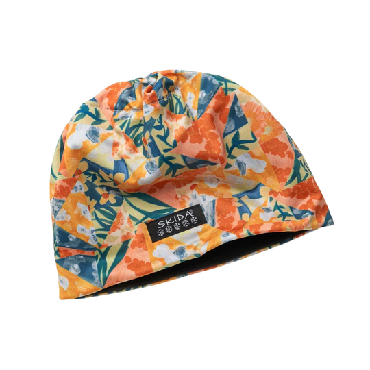 A knit beanie hat with a vibrant floral pattern in orange, yellow, teal, and white, featuring a black brand label that reads 'SKIDA'.