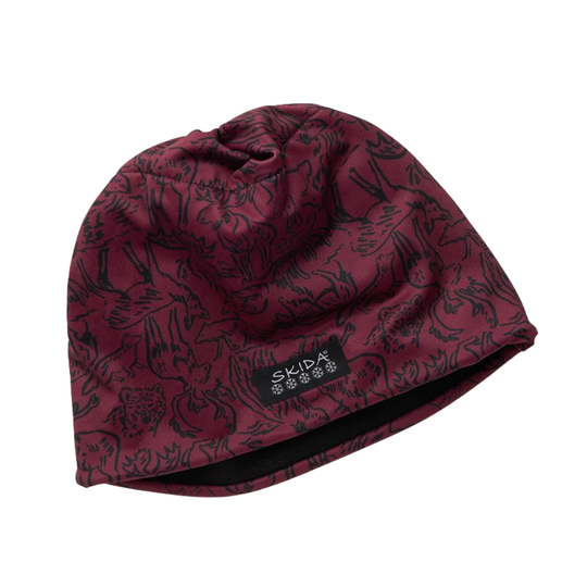 A knit beanie hat in a deep burgundy red with a black allover animal print pattern, featuring a black brand label that reads 'SKIDA' with snowflake icons. The beanie is photographed on a clean white background.