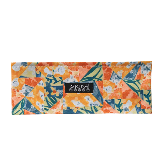 A rectangular fabric pouch with a colorful patchwork floral pattern in orange, yellow, teal, and white, featuring a black SKIDA brand label on the front, set against a plain white background.
