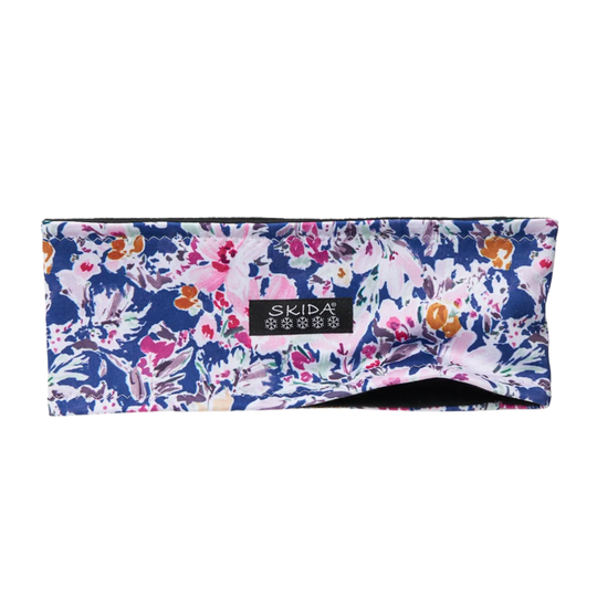 A wide fabric headband with a dense floral pattern in navy blue, pink, white, and orange, featuring a black brand label that reads 'SKIDA' with snowflake icons.