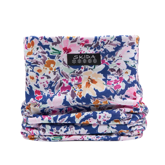 A folded fabric face covering or neck gaiter with a vibrant floral print on a navy blue background, featuring a black brand label that reads 'SKIDA'.