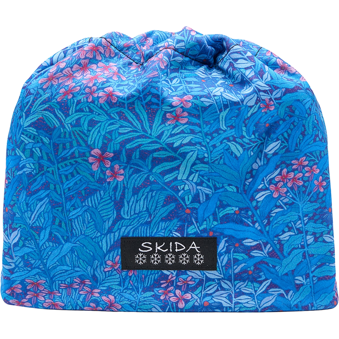 A blue knit beanie hat with a tropical floral and leaf pattern in shades of blue, teal, and pink, featuring a black SKIDA brand label on the front.