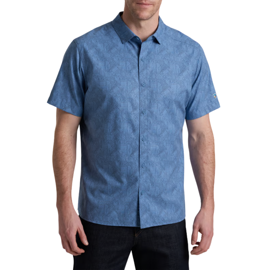 A man wearing a short-sleeve button-up shirt in a textured medium blue fabric, paired with dark jeans, against a plain white background.