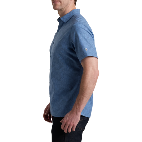 A man wearing a blue short-sleeve button-up shirt, shown in profile against a plain white background.