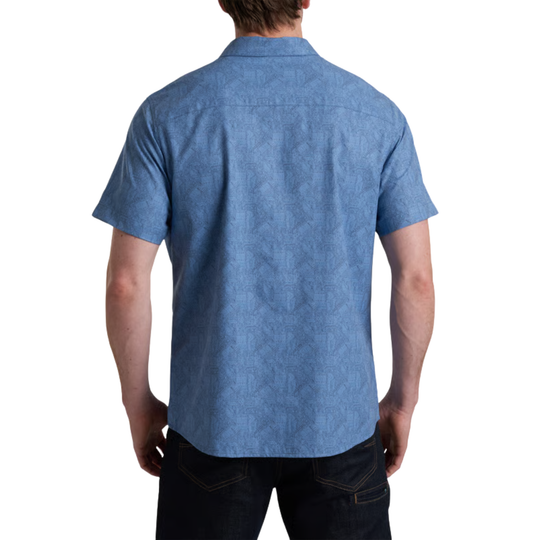 A man viewed from the back wearing a short-sleeve button-up shirt in a medium blue textured fabric, paired with dark jeans, against a plain white background.