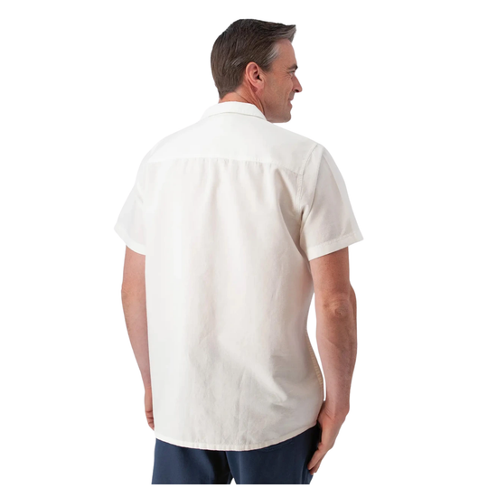 A man viewed from the back wearing a short-sleeve off-white button-up shirt and navy pants, set against a plain white background.