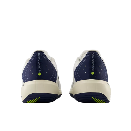 A pair of New Balance athletic sneakers shown from the back, featuring navy blue heel panels, white leather uppers, and a cream-colored midsole and outsole with lime green accents.