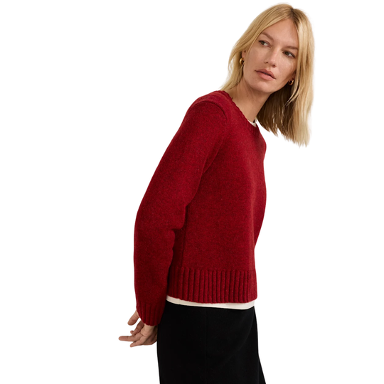 A blonde woman wearing a textured red knit sweater with a ribbed hem and cuffs, paired with black trousers, photographed against a solid white background.