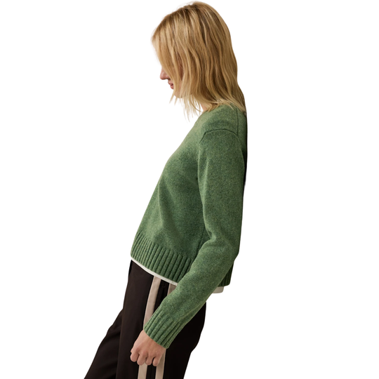 A woman shown in side profile wearing a cropped, heathered sage green knit sweater and dark pants with a light stripe, against a plain white background.