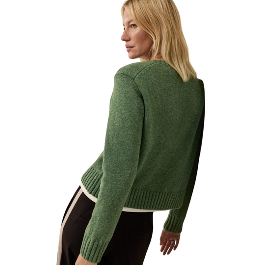 A woman shown from the back wearing a cropped green knit sweater with contrasting dark side panels and a white hem, paired with black pants with a white stripe, against a solid white background.
