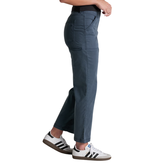 A side profile view of a person wearing dark slate blue cargo pants and white Adidas sneakers with black stripes, set against a plain white background.