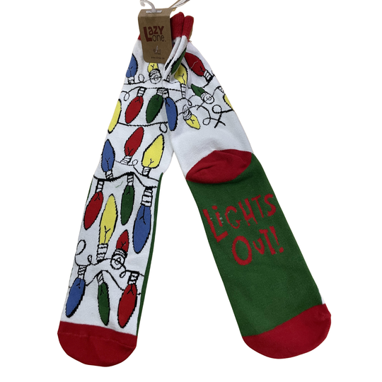 A pair of novelty Christmas socks hanging from a paper tag. One sock has a white background with a colorful string of light bulbs pattern, and the other has a green background with the words 'LIGHTS OUT!' in red.