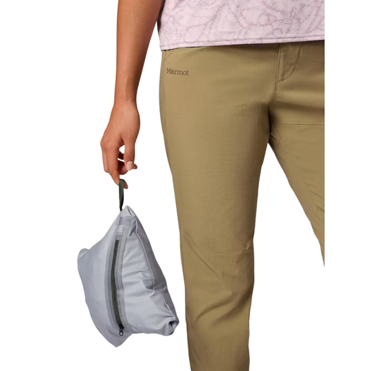 A person wearing tan Marmot pants holds a small light gray zip pouch against a plain white background.