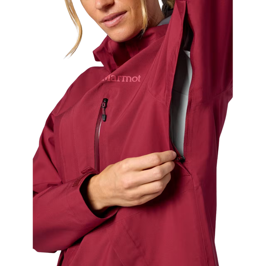 A close-up of a woman wearing a Marmot red waterproof jacket, demonstrating the high collar and a zippered pocket on the chest.