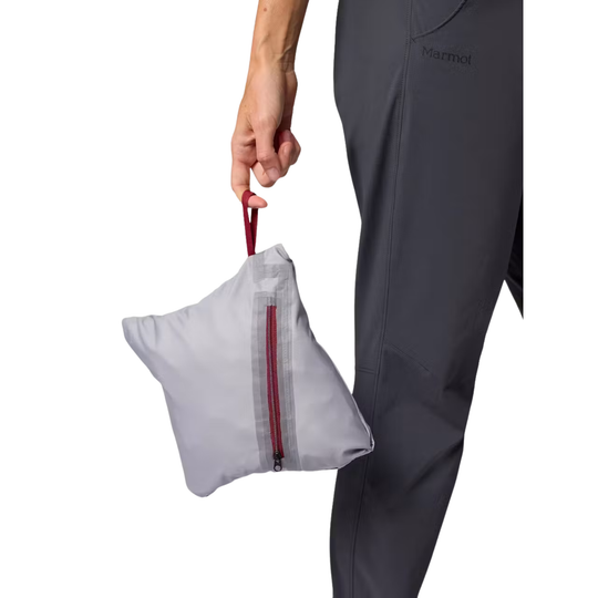 A person wearing dark gray Marmot pants holds a small light gray zippered pouch with a red zipper pull and red carrying loop against a white background.