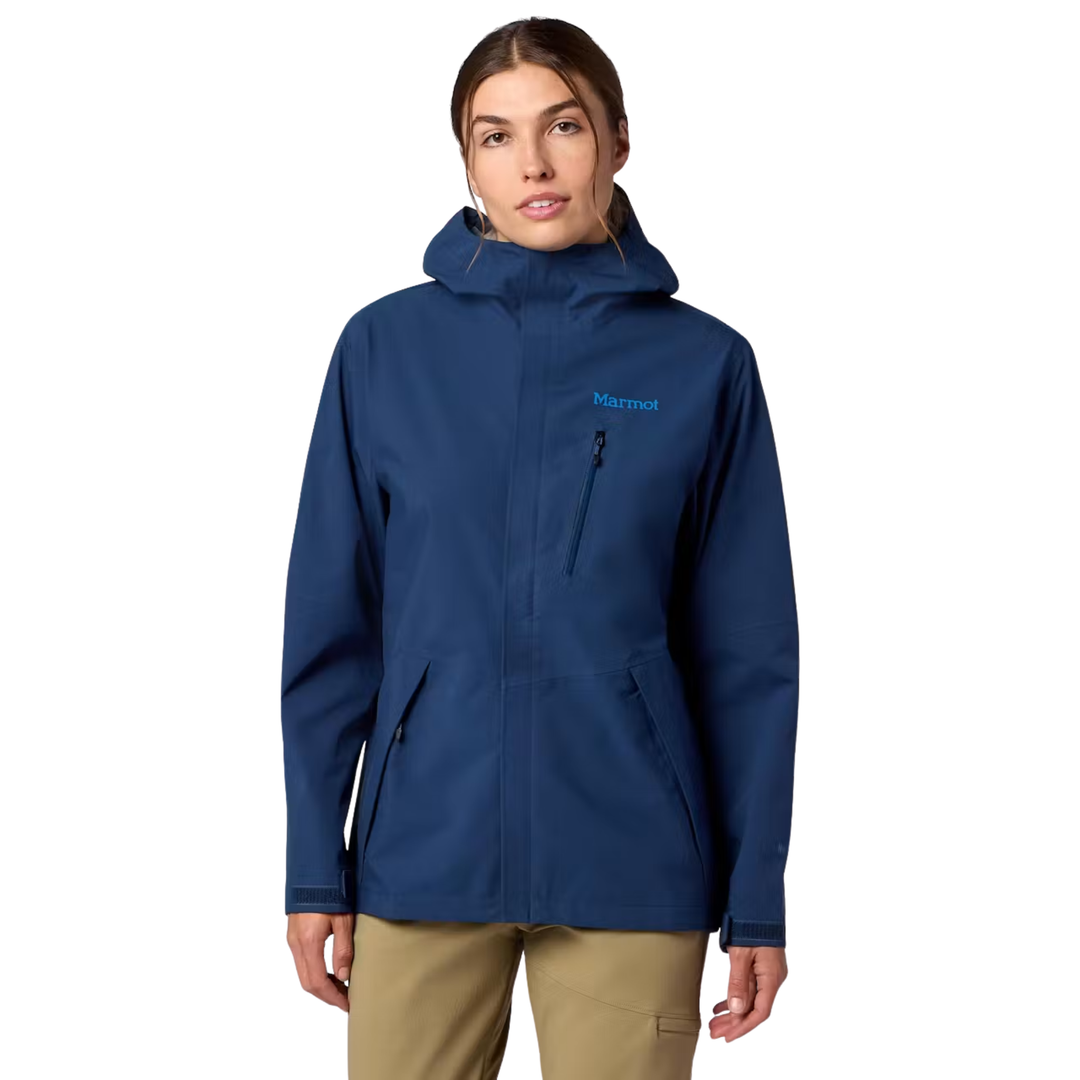 A woman modeling a Marmot hooded jacket in navy blue, paired with tan pants, against a plain white background.