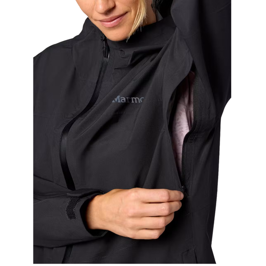 Close-up of a woman wearing a black Marmot jacket, opening the front zipper to reveal a light pink inner layer. The Marmot logo is visible on the chest.