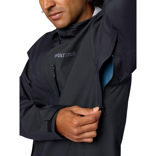 A close-up of a man wearing a black Marmot jacket, showing the brand logo on the chest and his hand unzipping the front pocket.