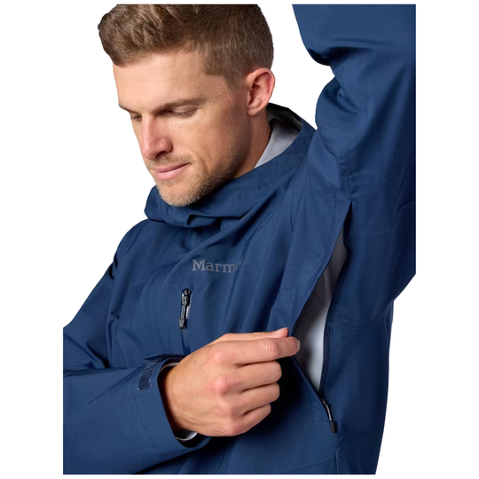 A man wearing a navy blue Marmot hooded jacket, shown from the chest up against a plain white background, opening the jacket's front zipper.