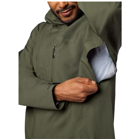 A close-up of a man wearing an olive green Marmot hooded jacket, demonstrating a side zippered pocket that opens to reveal a light-colored lining.
