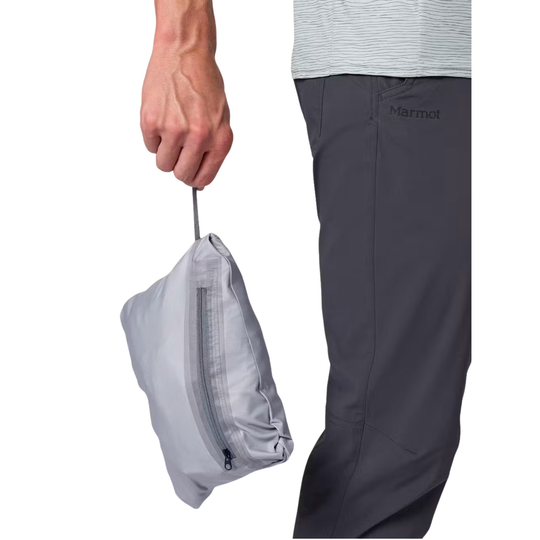 A person wearing dark gray Marmot pants holds a light gray zippered pouch against a white background.
