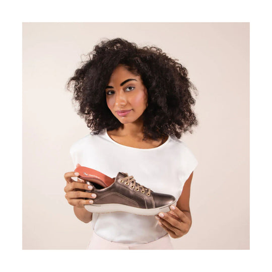 Brown lace-up sneaker with a white sole and tan eyelets held by a woman in a white top
