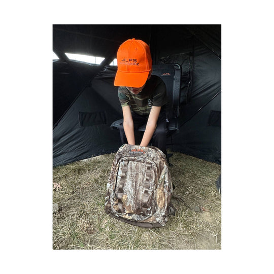 Camouflage backpack standing upright with multiple front pockets and shoulder straps