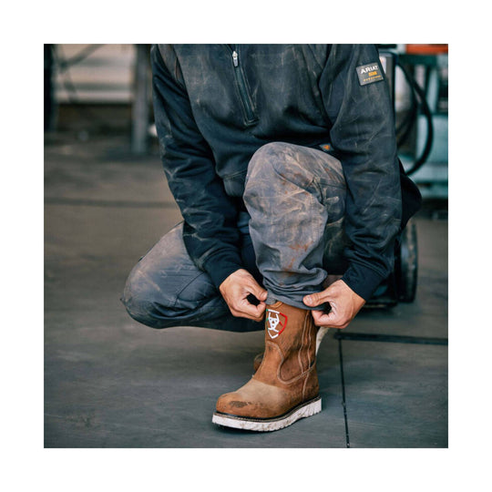 Worn gray work pants tucked into a brown pull-on work boot with a white sole