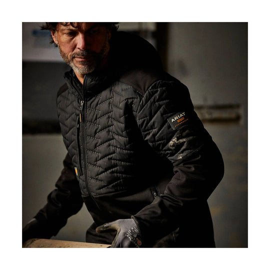 Black quilted work jacket with zip front, stand collar, and sleeve logo patch
