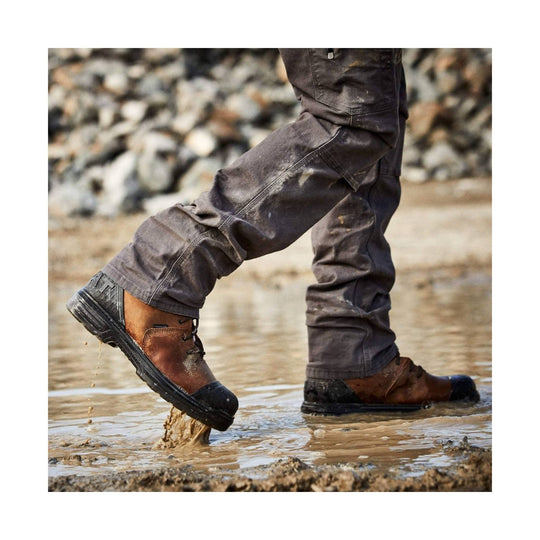 Brown leather work boots with black rubber toes and soles, shown walking through mud