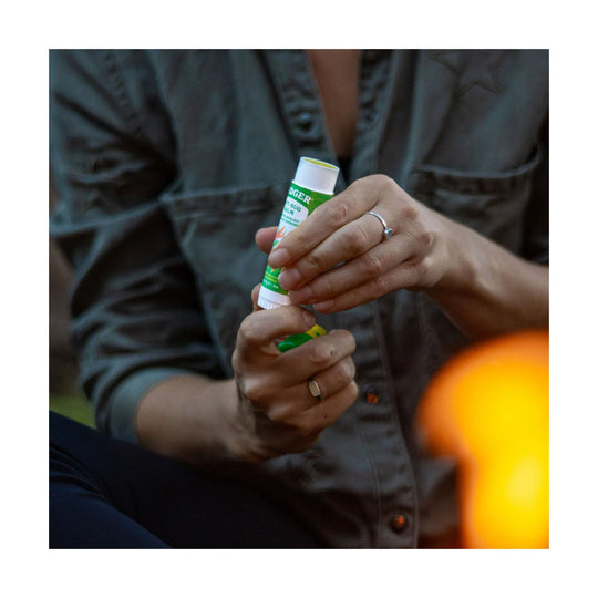 Green-and-white balm stick held in two hands, with a partially visible label and white cap
