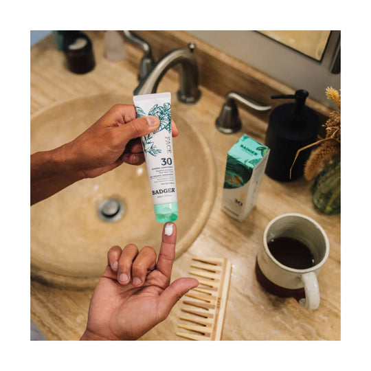Hand holding a tube of mineral sunscreen over a bathroom sink