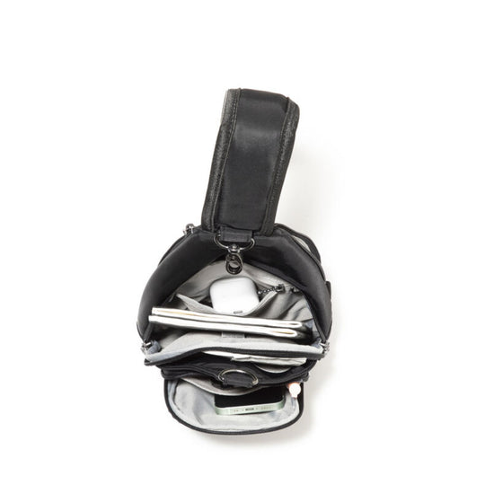 Black sling bag open to show a light gray interior, notebook, earbuds, and a phone.
