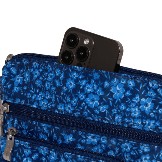 Blue floral crossbody bag with multiple zippered pockets holding a smartphone