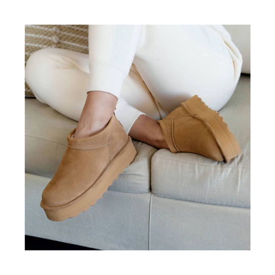 Tan suede ankle boot with thick platform sole, worn with white pants on a sofa