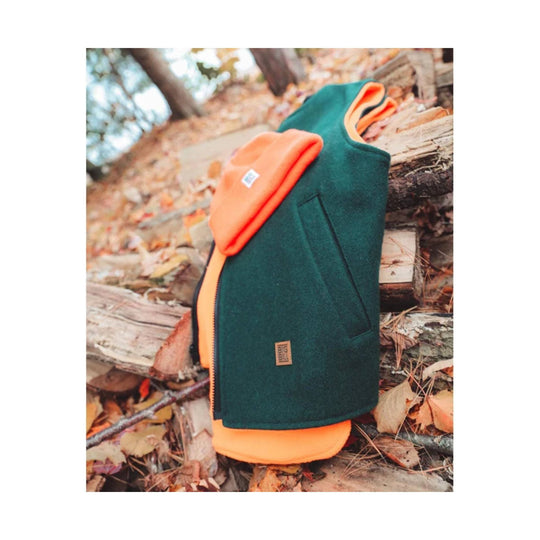 Reversible vest lay on wood log in the woods. Orange hat on top of vest.  