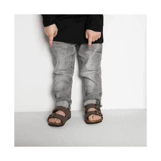 Brown double-strap sandals on a child wearing gray jeans