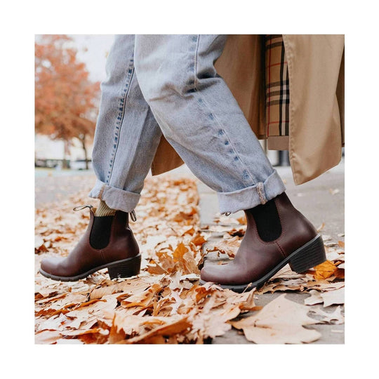 Brown leather Chelsea boots with low block heels, worn with cuffed jeans on a leaf-covered sidewalk