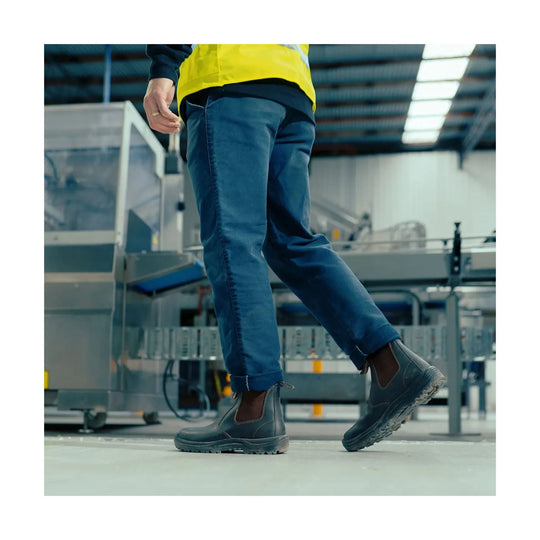 Person wearing blue jeans and dark shoes walking in an industrial setting