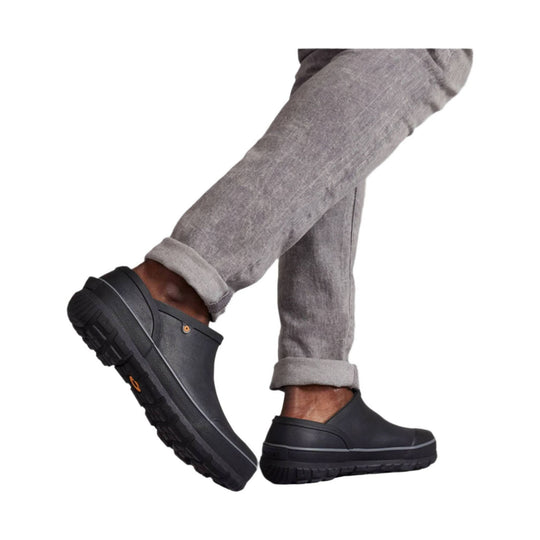 Black slip-on clogs with thick lug soles worn with rolled gray pants