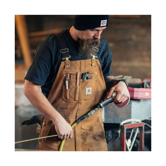 Brown duck canvas bib overalls with chest pockets, worn over a black shirt while using a sanding tool