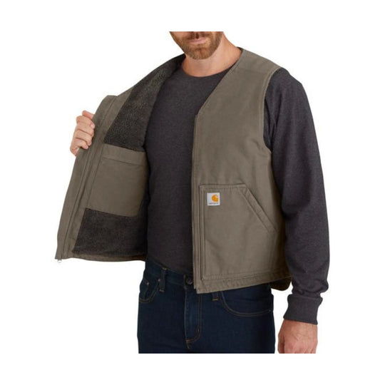 Brown sherpa-lined vest worn open over a dark long-sleeve shirt, with a front logo patch and zip pockets