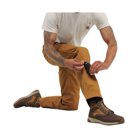 Brown work pants with reinforced front panels shown on a kneeling model, paired with brown work boots.