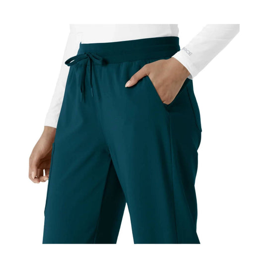 Teal boot-cut scrub pants with drawstring waist and side pockets, shown with a white long-sleeve top