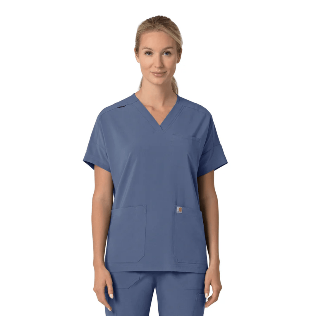 Blue V-neck scrub top with short sleeves and two front patch pockets, shown with matching scrub pants on a model.