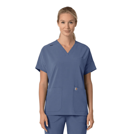 Blue V-neck scrub top with short sleeves and two front patch pockets, shown with matching scrub pants on a model.