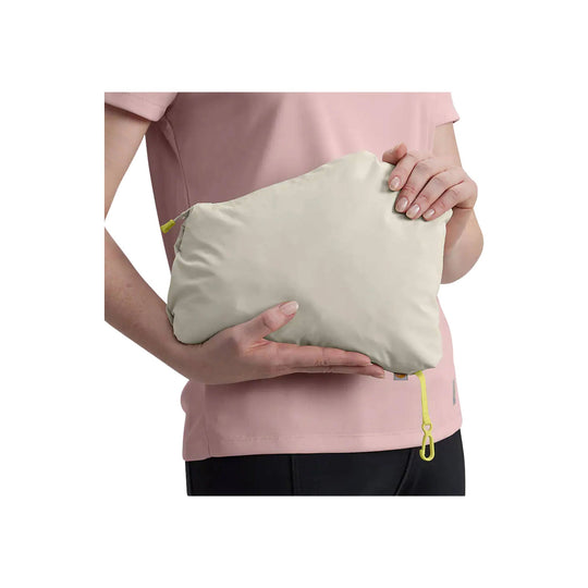 Folded light beige packable pouch held against a pink shirt