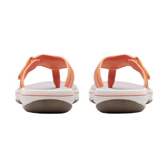 Pair of coral-orange slip-on sandals with white soles, shown from the back