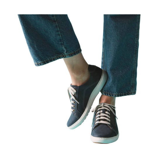 Navy lace-up sneaker with white sole, shown on crossed legs in blue jeans