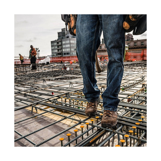 Brown leather work boots with orange laces worn with jeans on a construction site